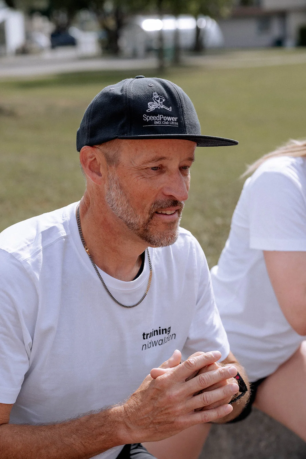 Hans-Peter mit Cap sitzt im Gespräch auf der Mauer