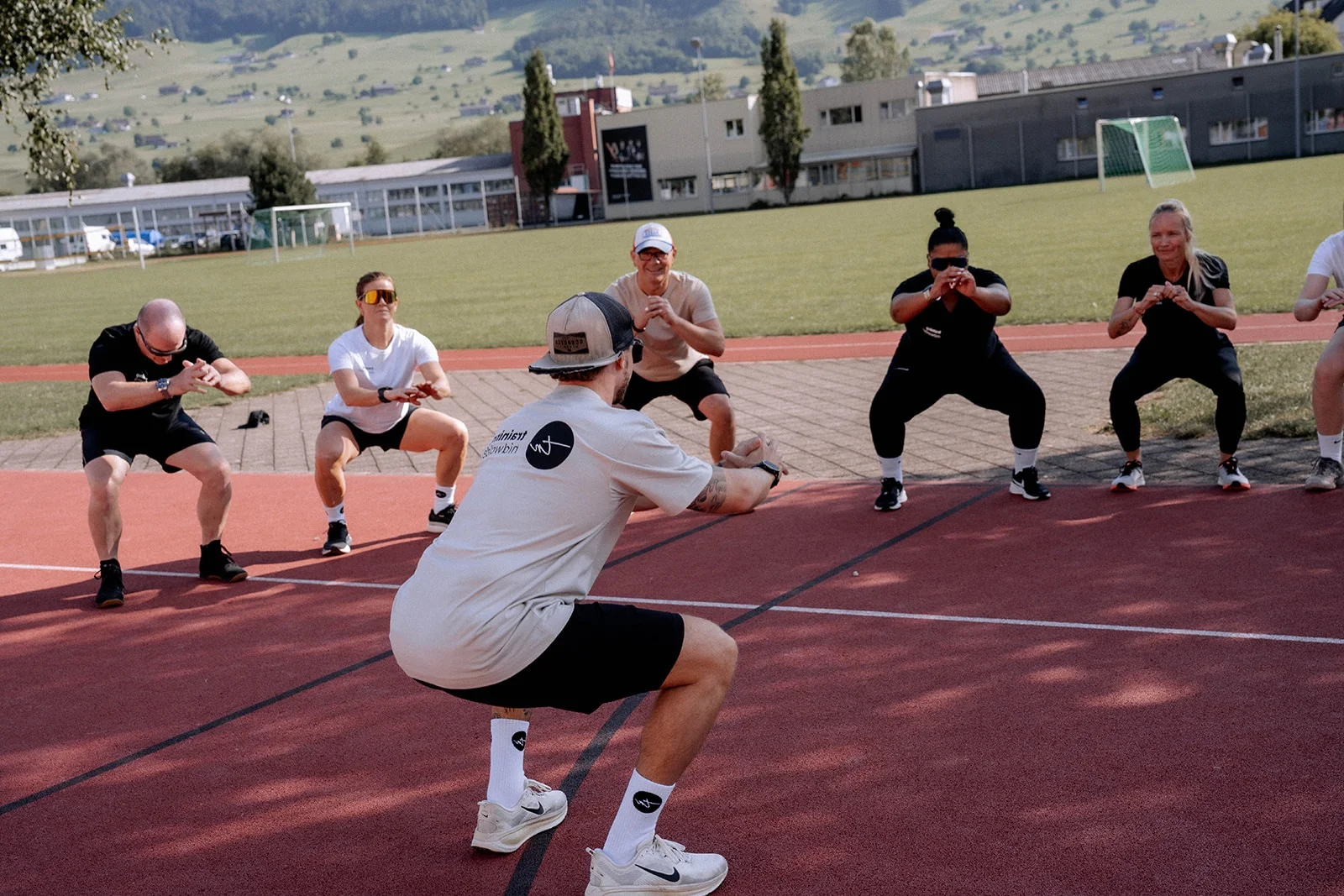 Ein Coach im training-nidwalden-Shirt macht auf der Laufbahn eine Kniebeuge vor, die Gruppe macht sie mit